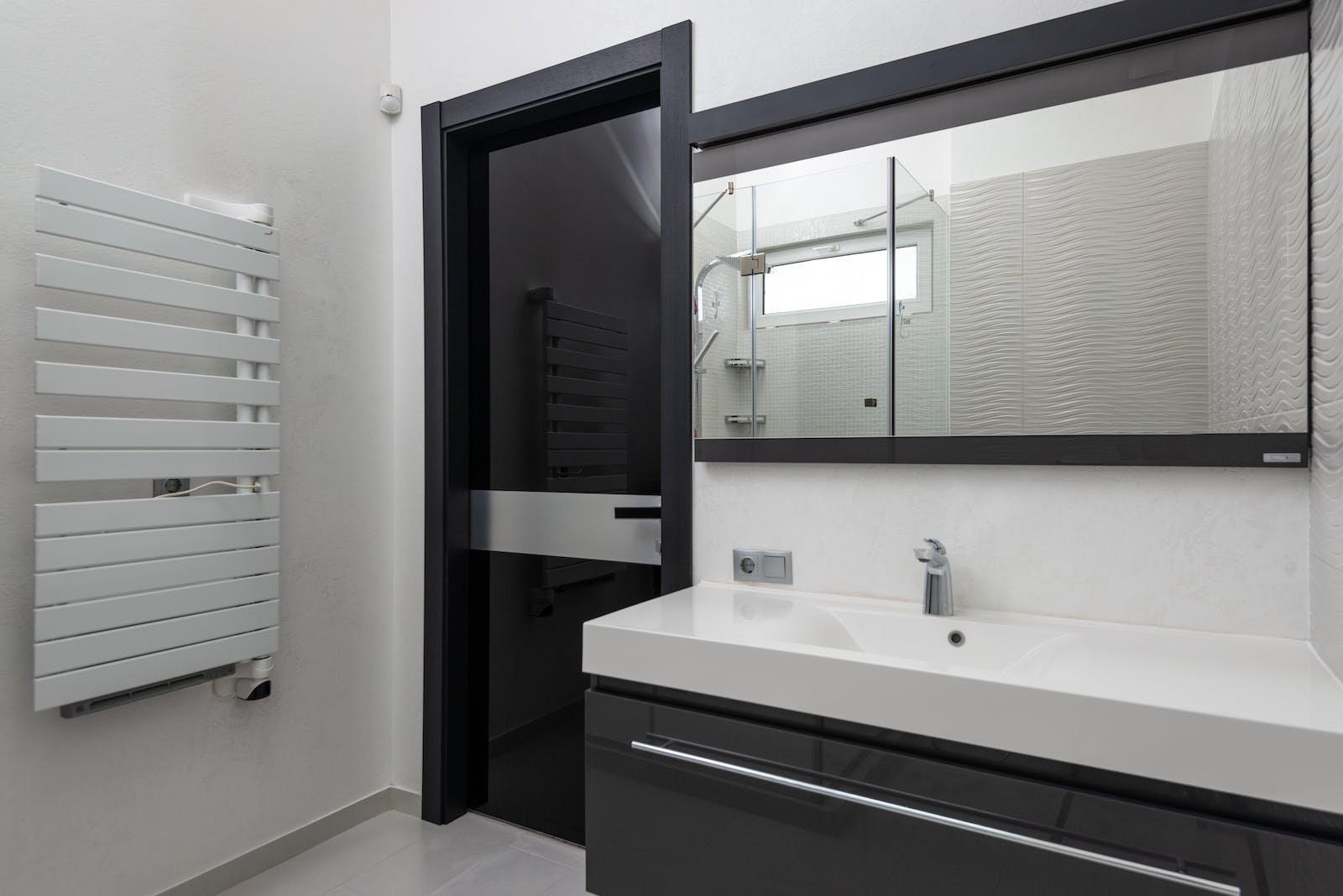 Creative design of bathroom with door between heated towel rail and washstand under rectangular mirror in light house